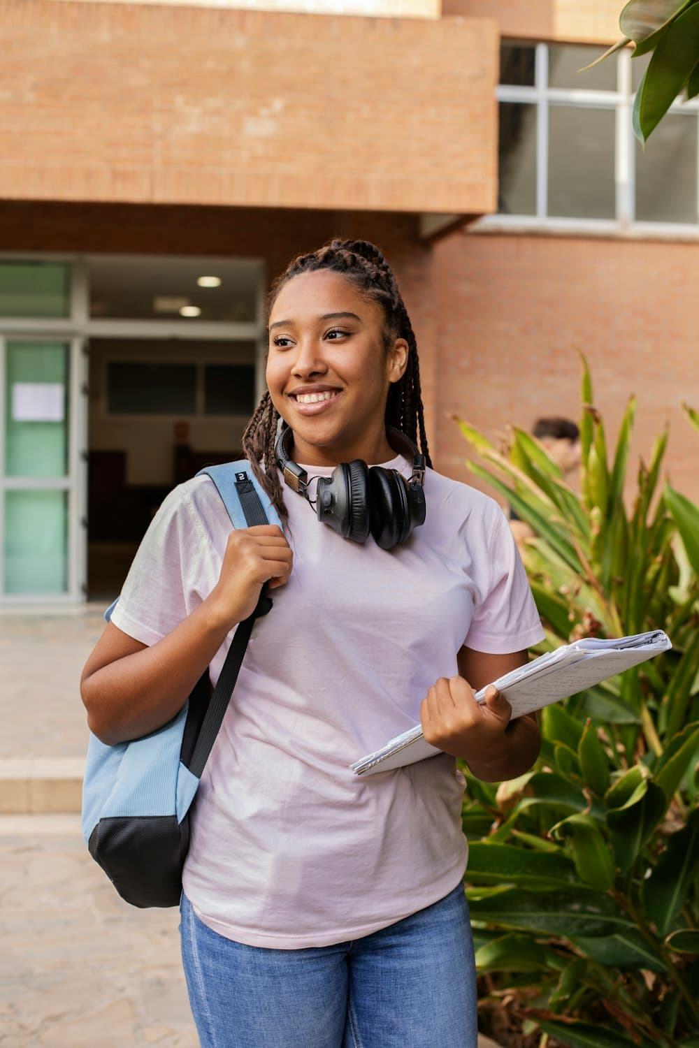 A smiling high school student with a backpack and notebook outside school
