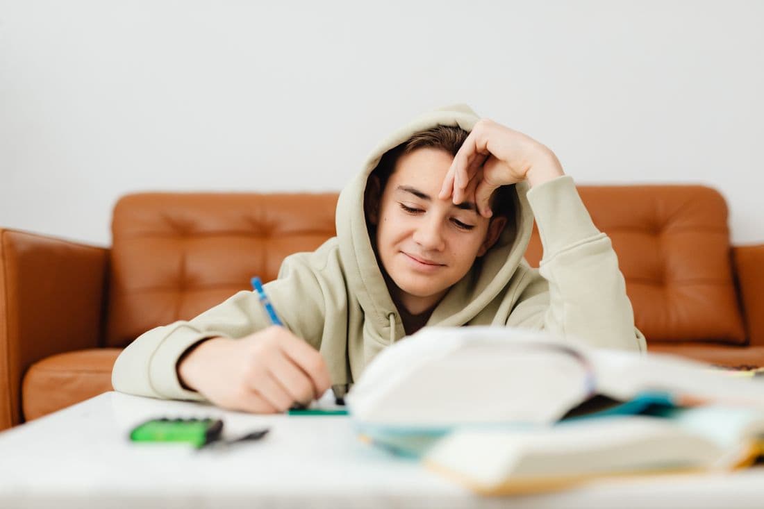 A high school student in a hoodie works through homework at home
